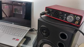Focusrite audio interface sat on top of a studio speaker next to a silver laptop