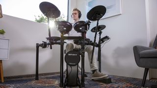 Man wearing headphones plays a Roland electronic drum set at home