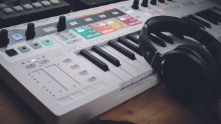 An Arturia Keystep Pro MIDI controller on a desk with some headphones